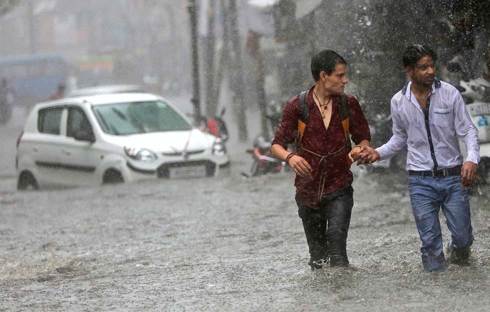 Zwei Männer kämpfen sich durch die überfluteten Straßen Indiens.