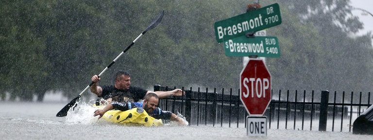 Zwei Männer rudern in Houston bei heftigem Regen auf einer überfluteten Straße in einem Schlauchboot.