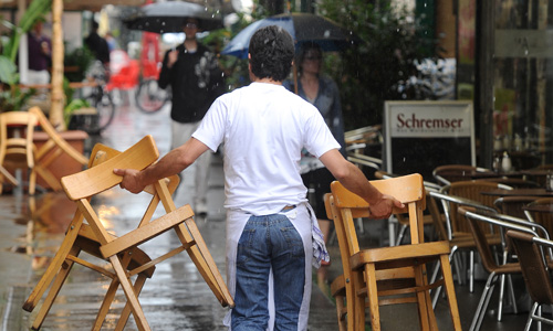 Mann räumt Stühle im Regen weg